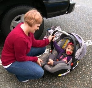 A cherubic baby, wrapped snugly in a soft blanket, sits contentedly in a car seat, tiny hands grasping at the straps. The car seat is securely fastened, ensuring safety on the journey ahead