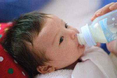 Newborn baby drinks her formula from the bottle while staring at her mom. Formula milk is popular. 