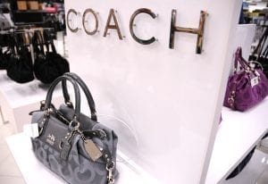 A stylish Coach bag displayed in a store, the brand's logo in the background, an elegant choice to give to fashion-conscious moms.