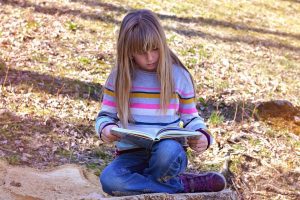 3rd grade child patiently reads one of her favorite books on a bright and sunny day.