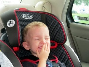 A child laughing while sitting in a car seat.