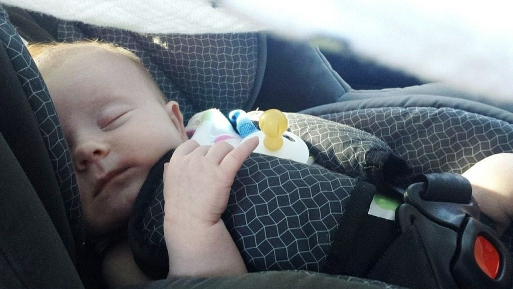 A cute baby snugly sleeps in a comfortable car seat with no cares in the world. Must have been dreaming of nice things. How content the parents might be. What joy to look at!