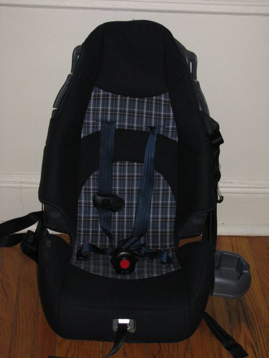 A high-back booster seat leaning on the white wall. This is an excellent choice for older children who have outgrown traditional car seats but still require a boost to ensure proper seat belt fit and optimal safety. 