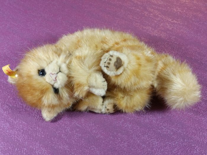 A cuddly smiling life-size stuffed toy cat. The faux-fur looks realistic making this stuffed toy looks real. The backround is color pink. 