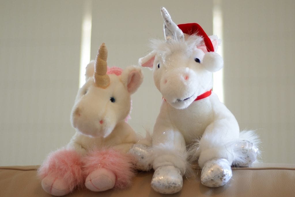 There are two smiling stuffed unicorns. The one on the left is pink and the other one is white. Their foot has a faux-fur. These lifesize toys look cute. 