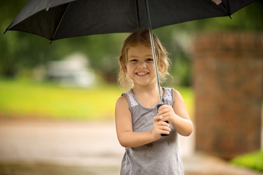 A kid having the best time playing during a rainy day. Make sure they have the right umbrella made properly for their own use.
