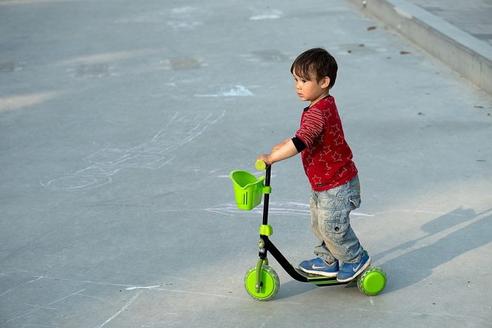 A toddler riding his best scooter in color green