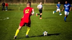 A youth playing football wears appropriate cleats. 