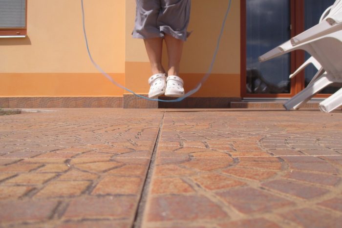 A person playing skipping rope outdoors on a bright day. 