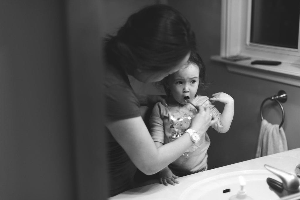 A mother holding a toothbrush brushes the teeth of her baby in the bathroom using one best baby toothbrush. 