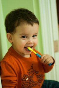 A kid holding his best colorful toothbrush. The toothbrush is yellow and blue. This colorful toothbrush attracts kids making toothbrush activities enjoyable. 