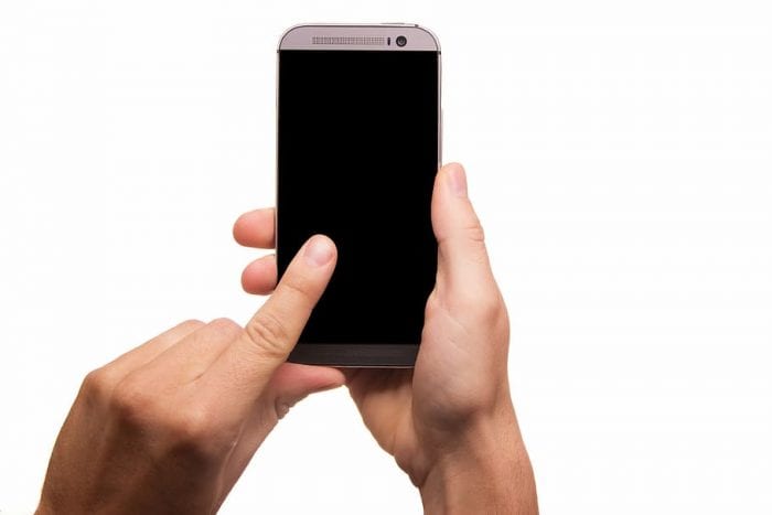 A hand delicately reaches out towards a modern smartphone's glossy screen.