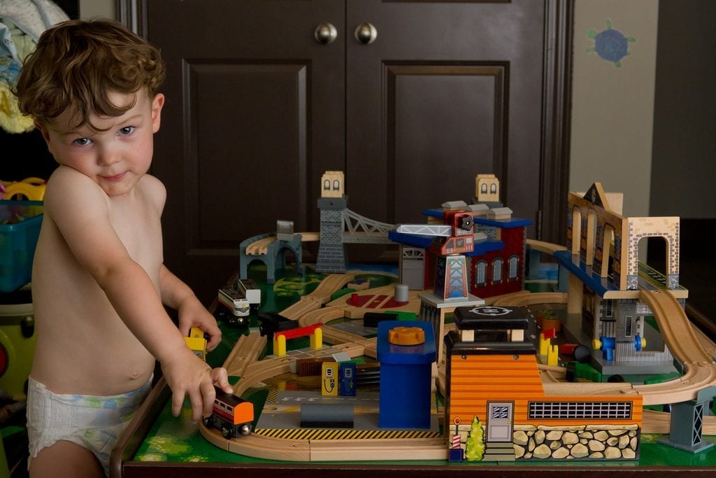 A kid wearing a diaper is playing his table train set. The size of the table is age appropriate.
