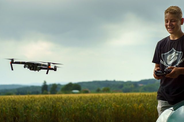 The boy is so happy as he plays with his cool drone in a big open area. He's good at controlling it with his fingers. The drone flies high up, moving smoothly and doing cool tricks. The picture looks like it has a nice humming sound as it moves around freely.
