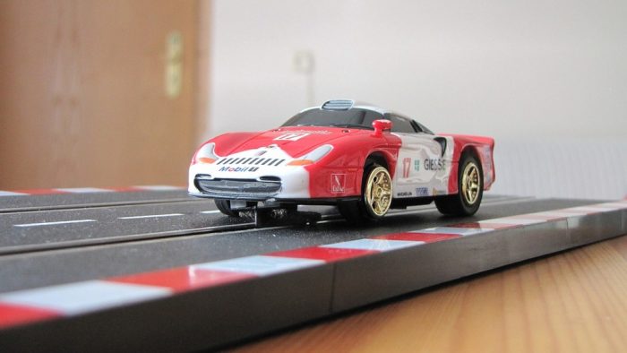 One of the quality car racing track toys in red and white color arranged on a brown floor inside the room.