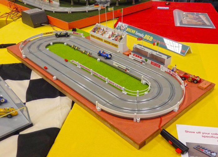 Two small race car toys on a toy race track placed on a colorful floor inside a brightly lit living room. 