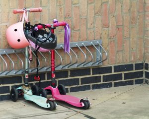 Kids' scooter and safety gears in vibrant girly colors parked in a garage corner. Two rides just being parked on the side of the house, ready for use the next day.