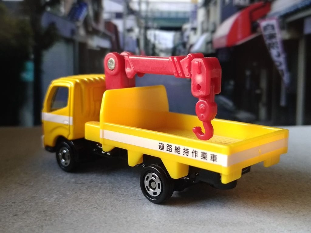 Toy Truck: A toy tow truck for kids with a bright yellow and red crane on a miniature city street background.