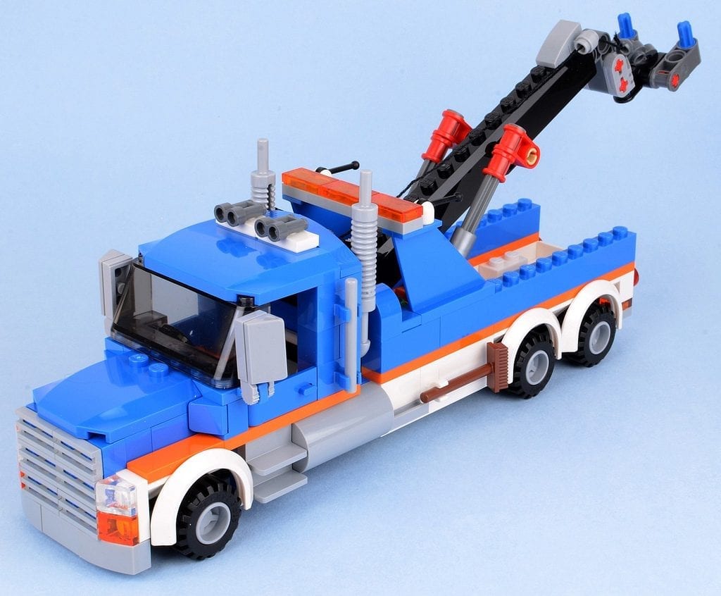 Toy Tow Truck: Blue and orange toy tow truck made from building blocks on a blue background, designed with a working crane and playful details.