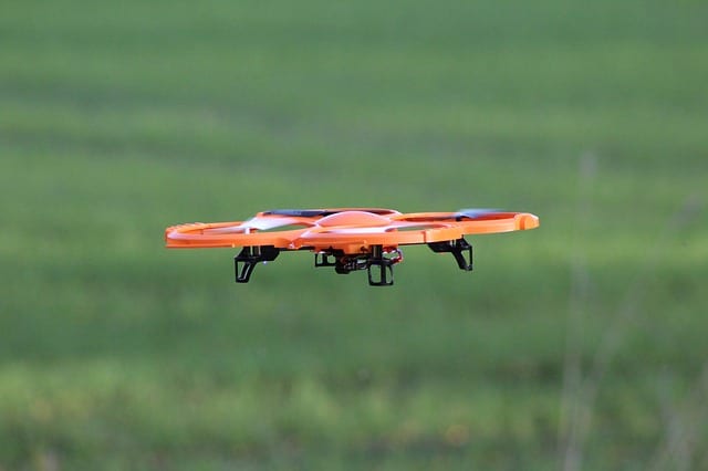 Best toys for eleven year olds: Orange drone flying in the air for a green grassy background.