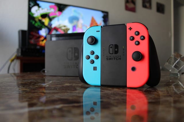 Nintendo Switch: A cool toy and interesting toy for an 11 year old boy. Best toys for eleven year old: Nintendo Switch console with blue and red Joy-Con controllers in front of a TV with a game on the screen.