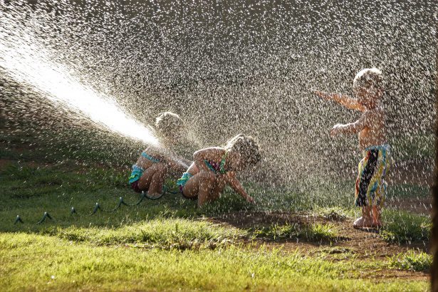 The kids are playing with the best sprinkler outside their house. 