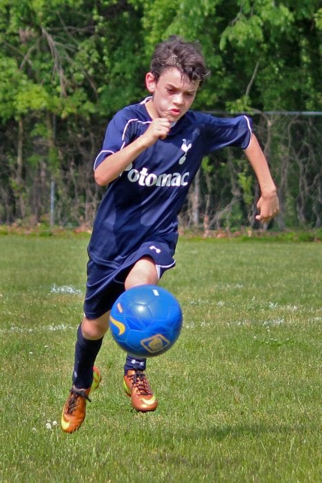 Young soccer player in a dark blue jersey controlling a blue soccer ball on a green field.