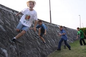 Joyful thirteen year old boys engaged in outdoor play, walking and balancing on a slant wall for fun. Their vibrant energy and carefree spirits shine through as they navigate the inclined surface, creating a heartwarming scene of youthful exuberance and shared adventures for life.