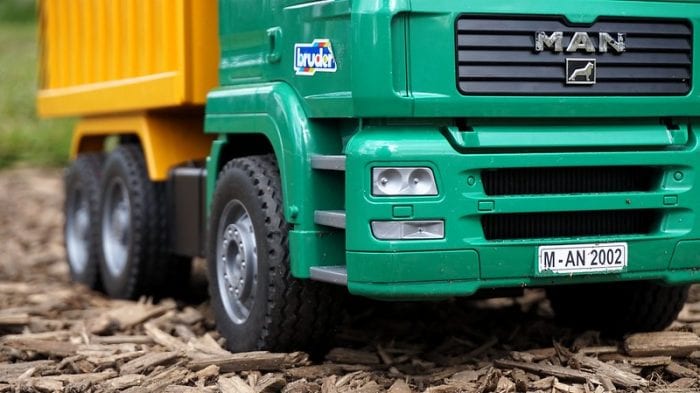 Toy Tow Truck: Green and yellow toy dump truck on a bark mulch surface, designed for outdoor play for children.