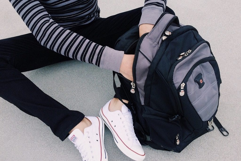 Person seated on the ground with a gray and black backpack beside them, ideal for carrying nursing school supplies.