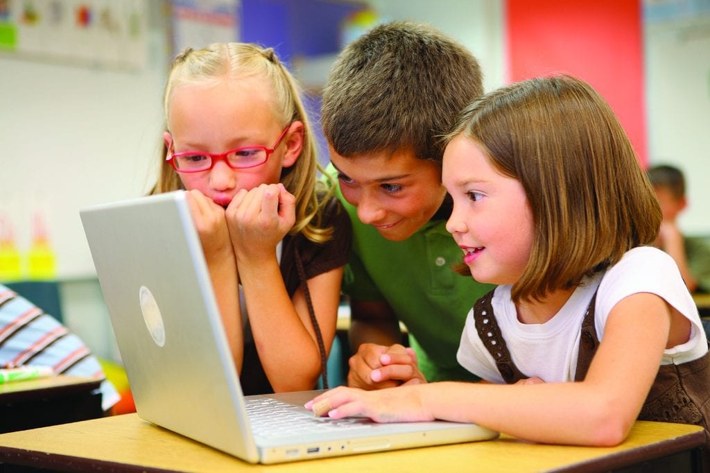 Three kids, two girls and one boy, are navigating the internet through their laptop and were looking some fun sites while facing the computer