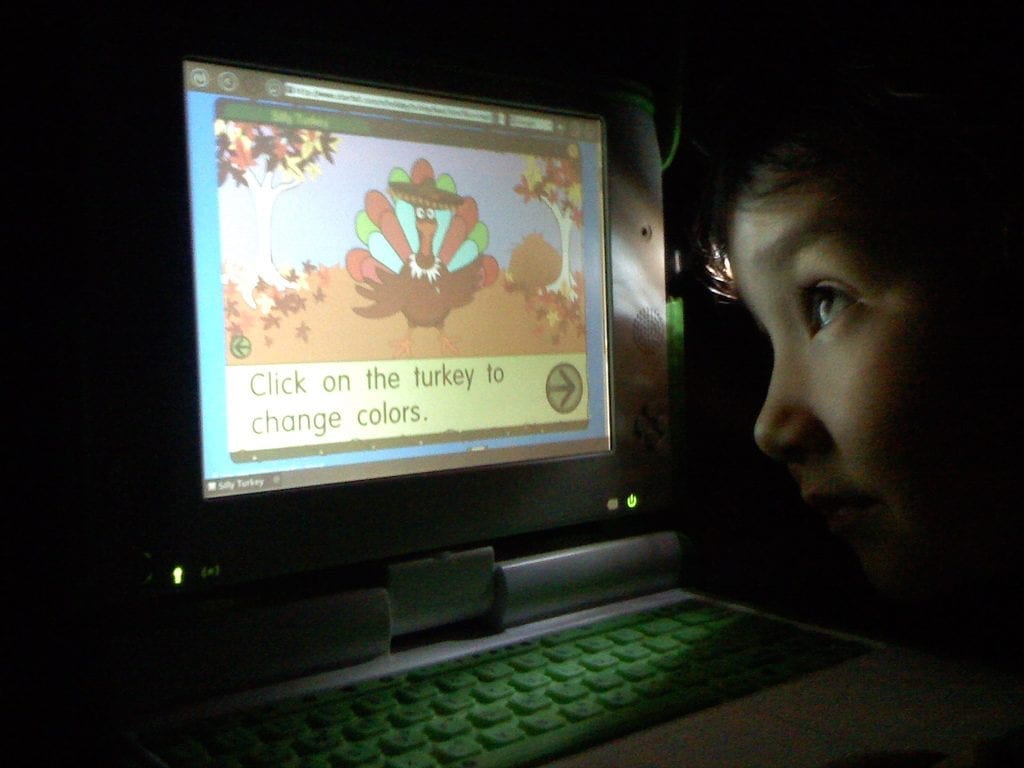 A child is reading a text on the screen of his laptop while his eyes are too close on the screen