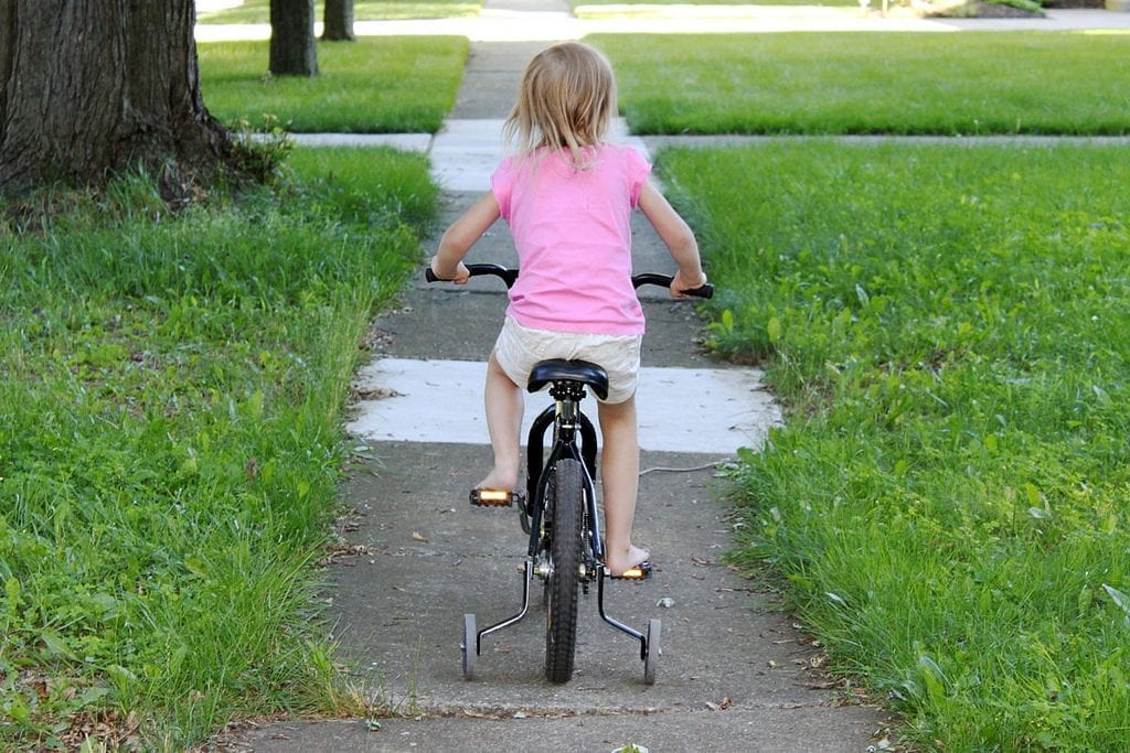 A girl wearing a pink shirt bikes outdoors on a bright day.