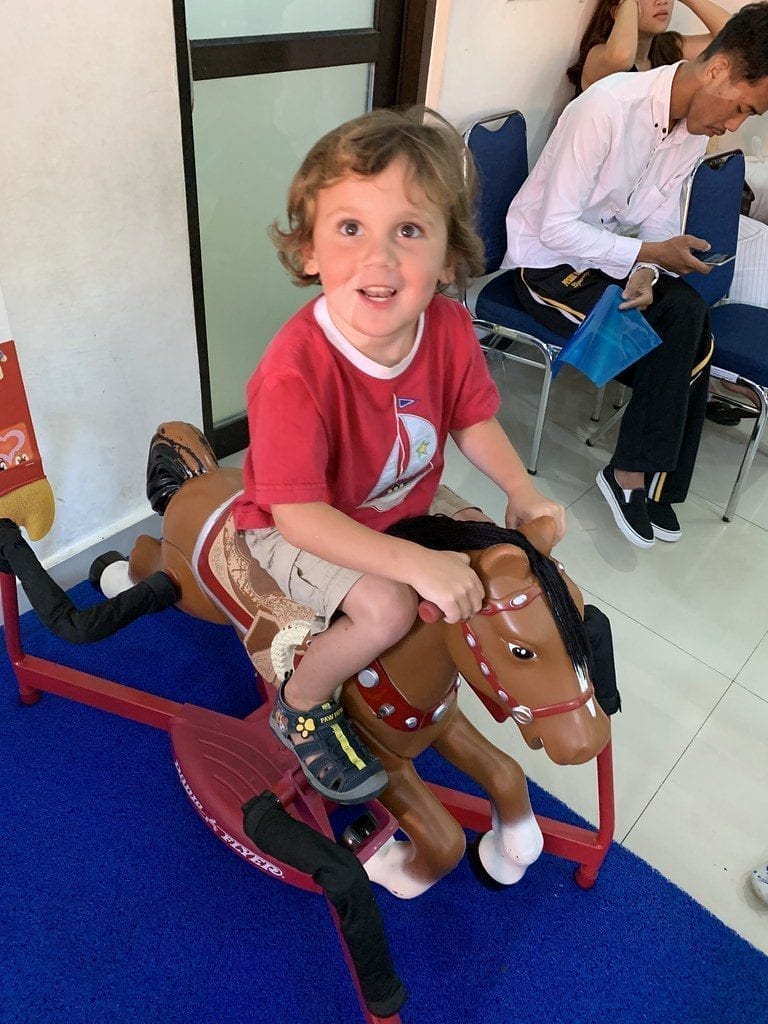 A boy riding a spring rocking horse while waiting for his mama.