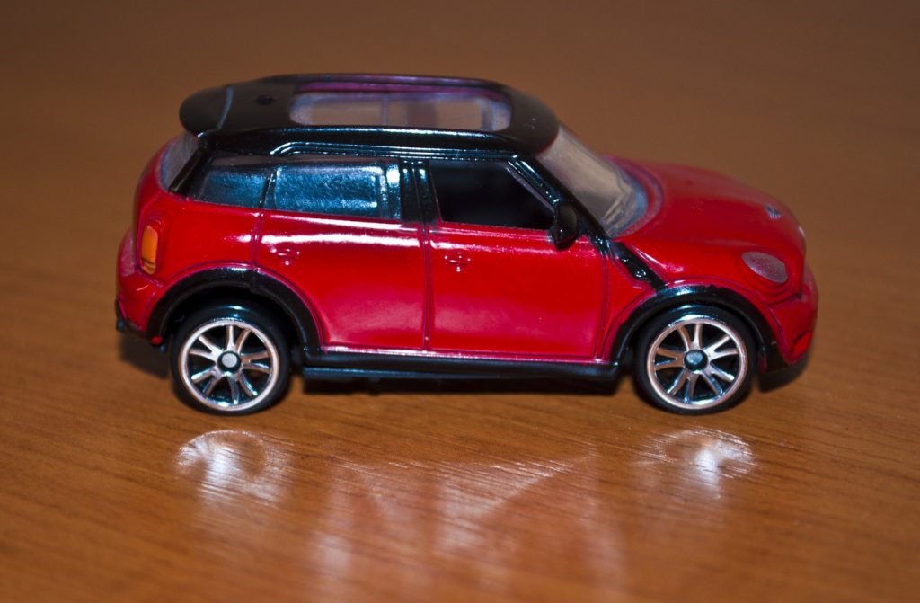 A close-up of a toy car, best for toddler playtime, with a shiny red finish and detailed design, parked on a wooden surface.