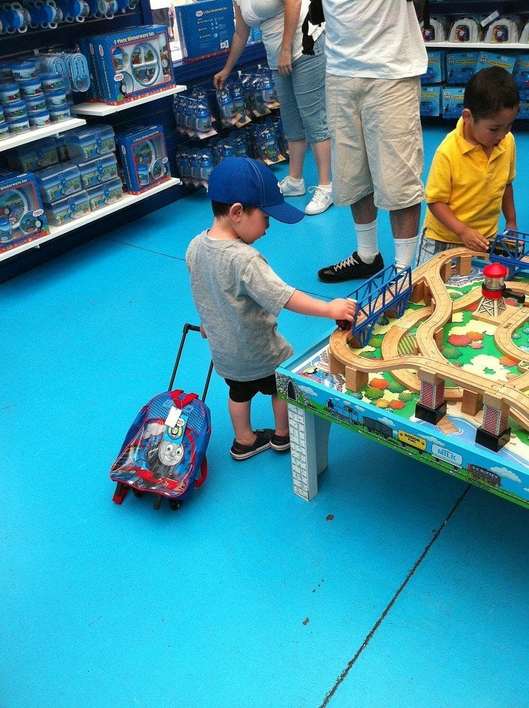 A boy holds a play set while shopping for Imaginarium metro line train table with his parents. 