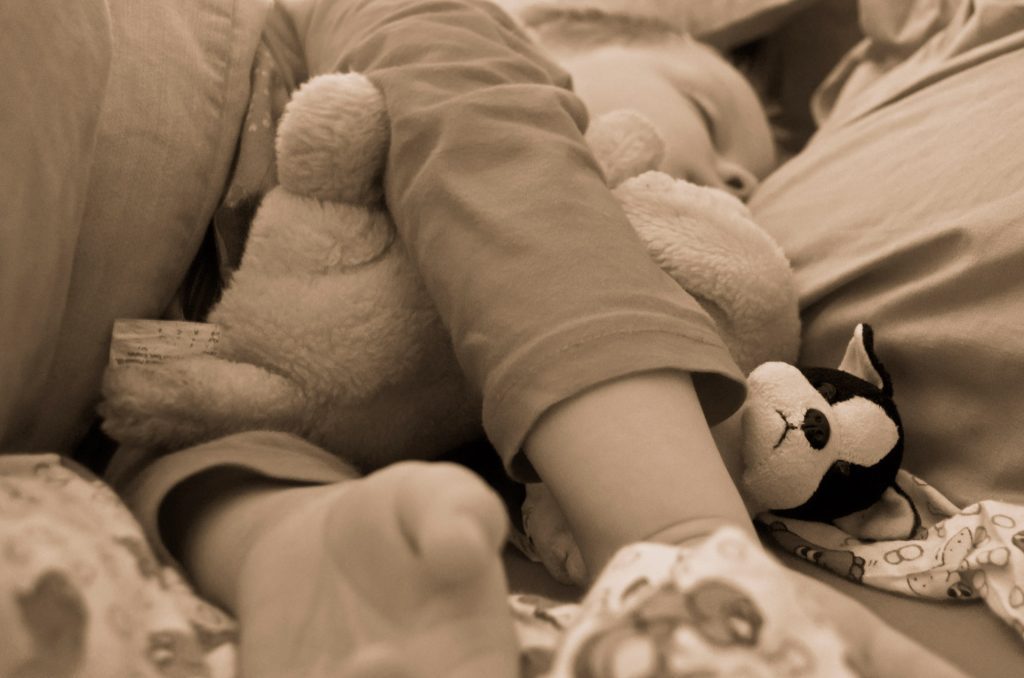 A picture of a kid hugging some plushies. The picture has a sepian filter effect.