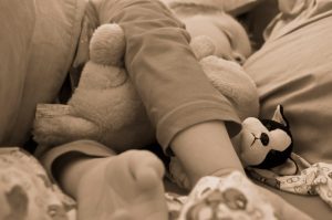 A sepia-toned image of a child napping with a plush animal by their side.