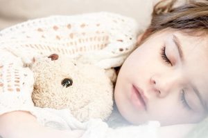 Baby girl sleeping with her stuffed teddy bear.