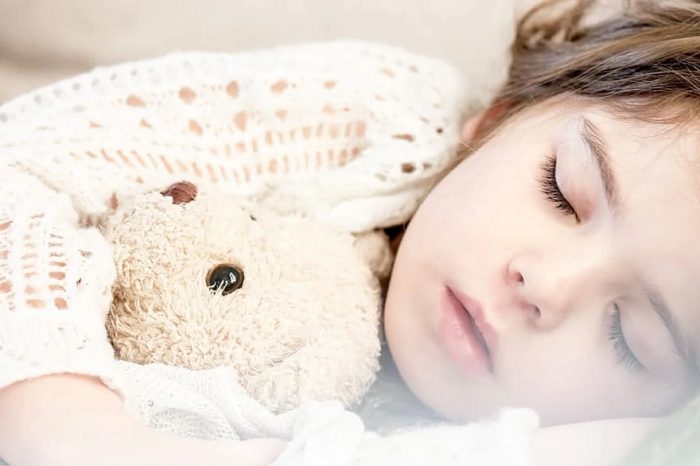 Baby girl sleeping with her stuffed teddy bear.