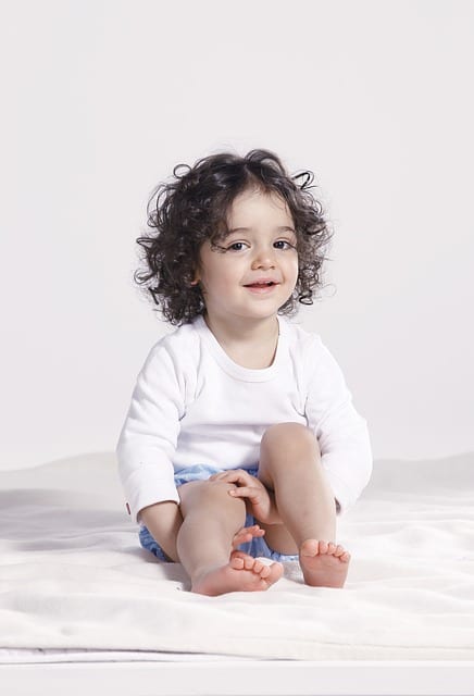 smiling 22-month-old baby with curly hair sitting down and looking at the camera