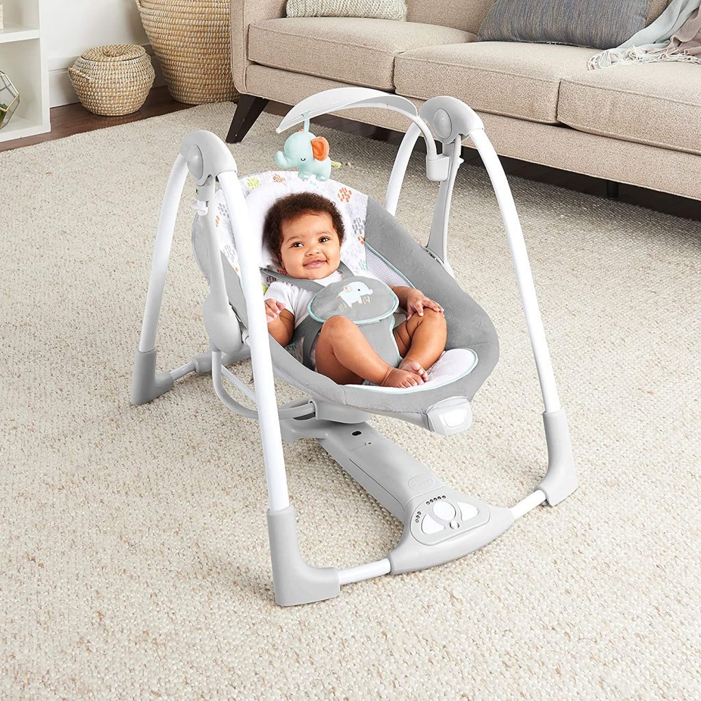 A cute infant is smiling while riding the gray-color swing in the dining room.