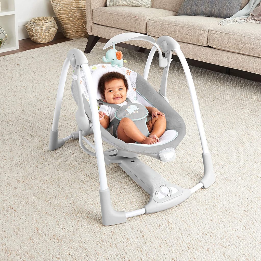 A cute baby is smiling while riding the gray-color swing in the dining room.