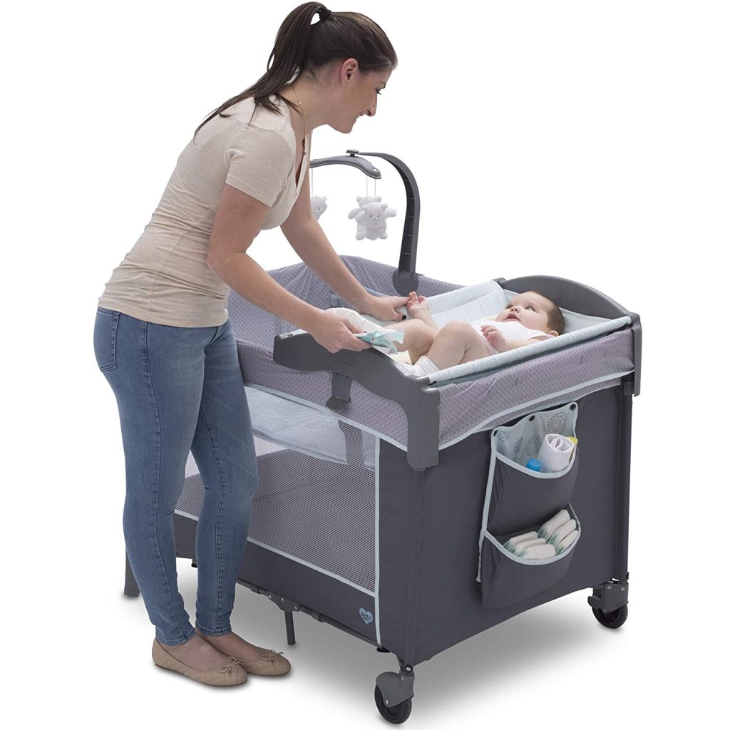 A mother attending to her baby on a portable pack n play crib with a diaper changing tray. This pack n play is gray.