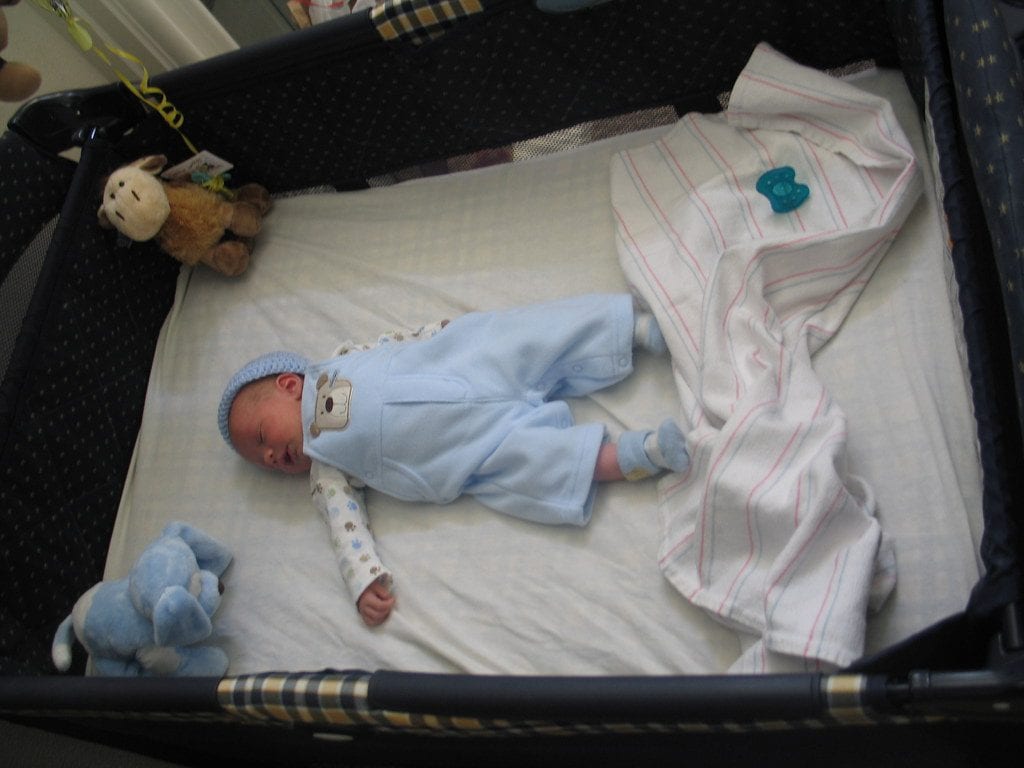 A baby peacefully sleeping on his portable pack n play crib.