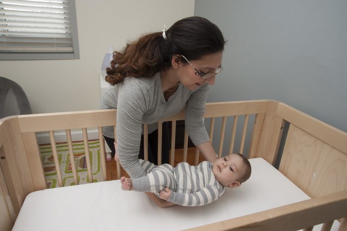 Cot for babies. A mother gently lays her son on the comfortable cot, ensuring a peaceful sleep for her little one.