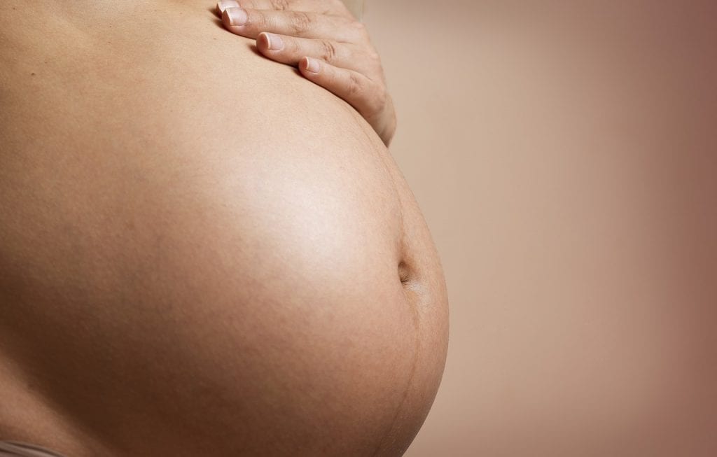 A mother is holding her baby bump with her hand while wearing a Maternity Underwear.