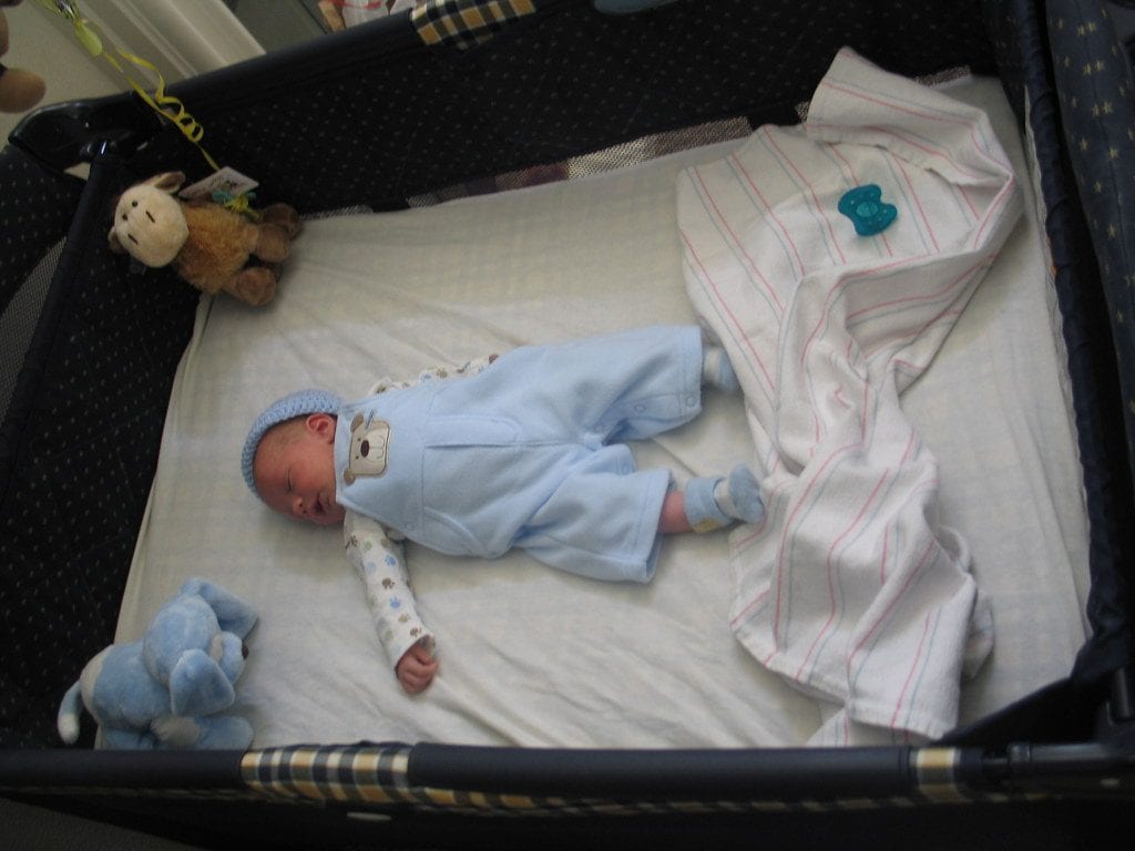 A cut newborn baby in a crib with stuffed toys. 