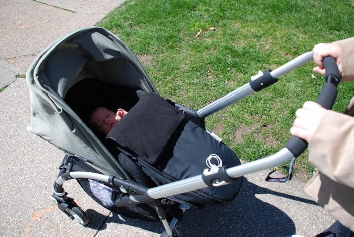 Bugaboo Bee Review: A baby peeking out from a Bugaboo Bee stroller on a sunny pathway with green grass on the side, showcasing the Bugaboo Bee comfort and style.