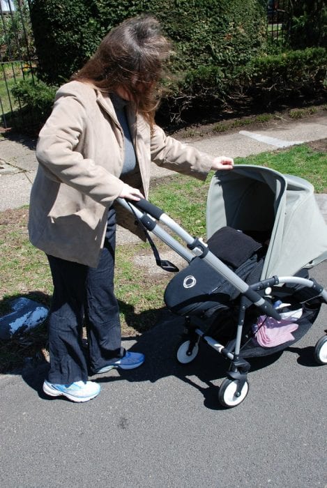Bugaboo Bee Review: An individual tends to a Bugaboo Bee stroller in a park setting, with trees and a clear blue sky in the background, emphasizing that the Bugaboo Bee has a practical design.